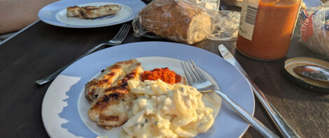 Auf einem Teller liegt ein gegrilltes Stück Hähnchenbrust, etwas Kartoffelsalat und ein kleiner Löffel Ajvar.