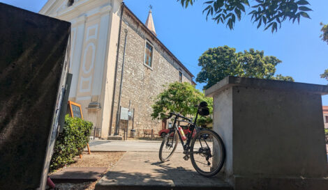 Ein an eine Mauer gelehntes Fahrrad im Schatten vor einer Kirche.