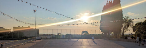 Ein betonierter Fußballplatz einer Grundschule vor einer untergehenden Sonne.