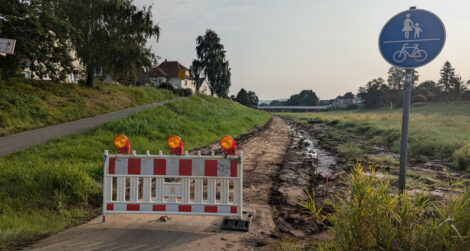 Ein Weg durch eine grasbewachsene Mulde. Die Oberfläche ist blanke Erde, da augenscheinlich das vorher dort befindliche  Pflaster entfernt wurde.