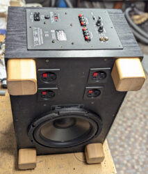 Ein hochkant stehender Subwoofer. Man sieht das große Basschassis und auf der Frontseite das Aktivmodul.