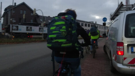 Einige Schüler fahren auf einem schmalen benutzungspflichtigen Radweg. Der daneben liegende Gehwegteil ist von einem Bulli zugeparkt, so dass die verbliebene Fläch auch noch schlecht zu nutzen ist.