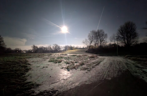 Ein Geh- und Radweg in einer Mulde ist zunächst überflutet worden und dann übergefroren. Über das Eis mit vielen Lufteinschlüssen blickt man auf einen sehr hellen Vollmond, welche die Szene in eine eisiges Licht setzt.