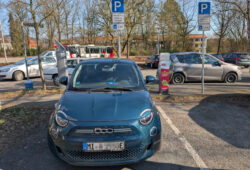 Ein grüner Fiat 500e lädt an einer Ladesäule, welche mit "Parkscheib, 4 Stunden während des Ladevorgangs" beschildert ist.