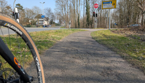 Der Blick aus Höhe der Fahrradnabe eine Fahrrades auf die sehr unebene Oberfläche eines viel zu schmalen, benutzungspflichtigen, kombinierten Geh- und Radweges.